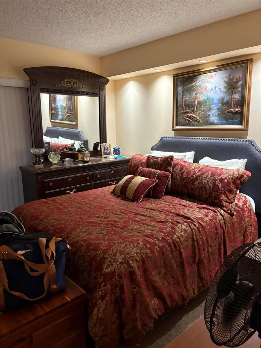 A bedroom features a dark wood dresser with a mirror, a bed with red bedding, and landscape art — 3 Kent A, West Palm Beach FL 33417, WEST PALM BEACH, FL