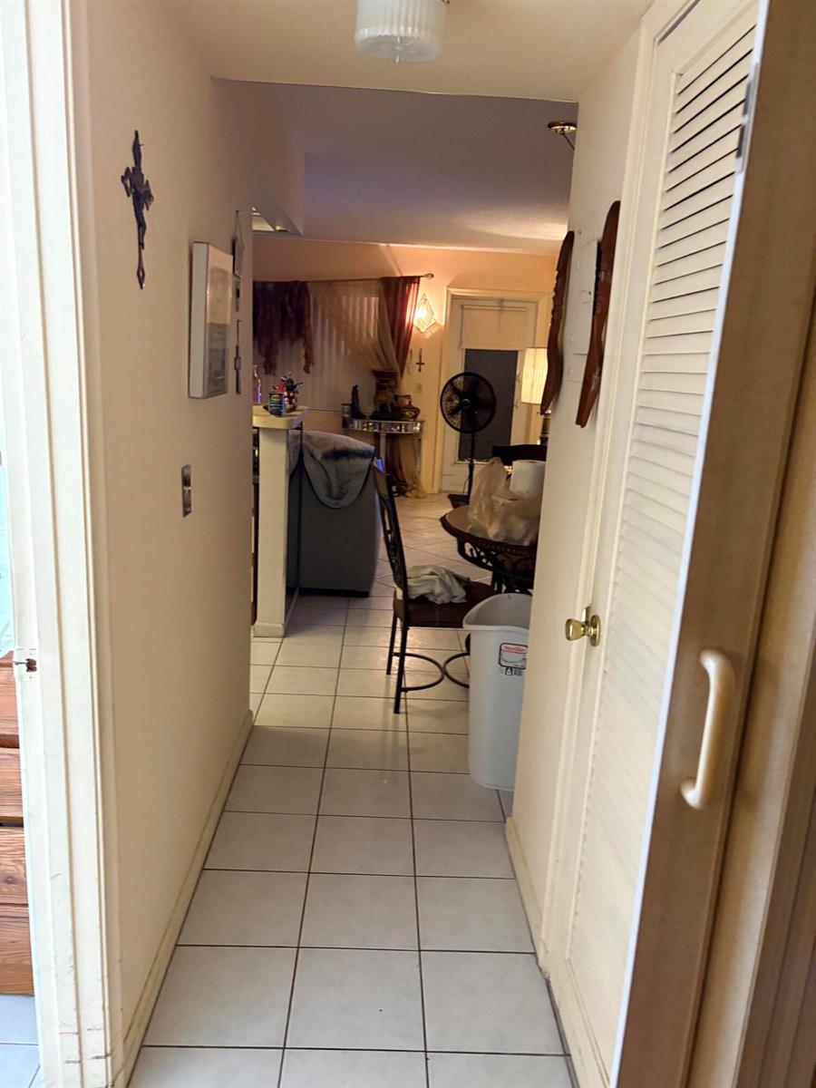 A hallway with white tile flooring leads into a living area with a dining table — 3 Kent A, West Palm Beach FL 33417, WEST PALM BEACH, FL