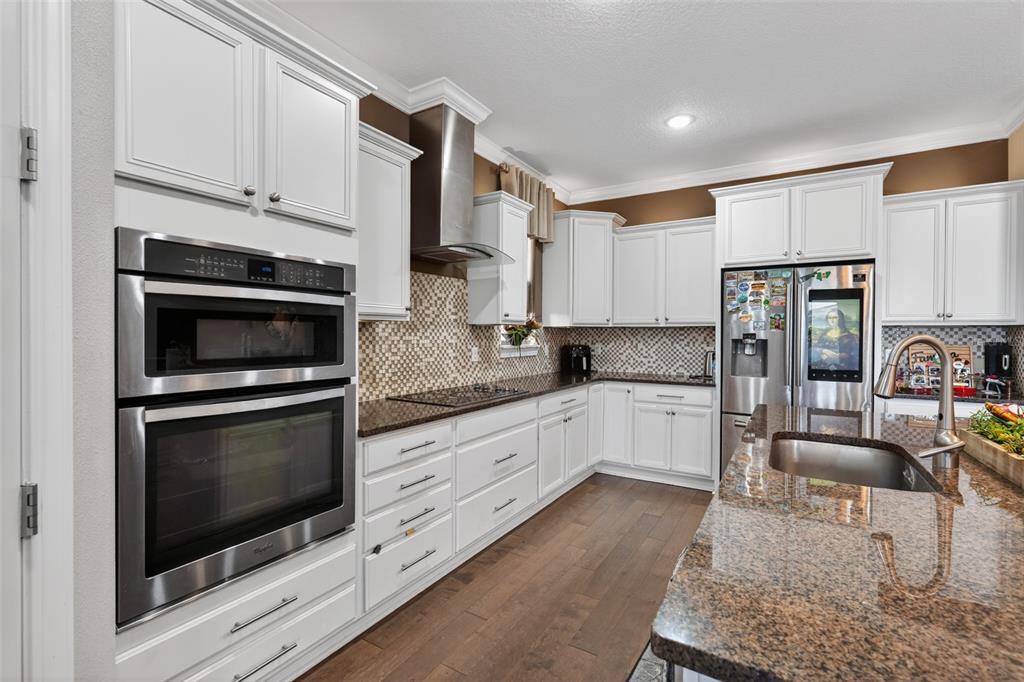 A kitchen with white cabinets, stainless steel appliances, granite countertops, and dark wood flooring — 5088 HARTWELL COURT, ST CLOUD, FL
