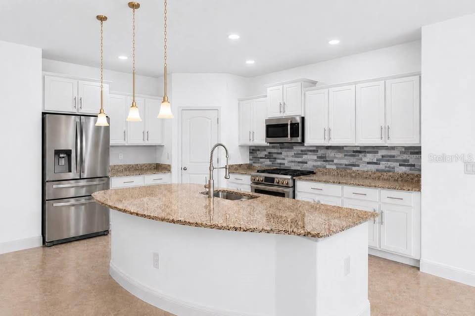 A kitchen features white cabinets, granite countertops, a center island, and stainless steel appliances — 1316 LAKE BATON DRIVE, DELTONA, FL