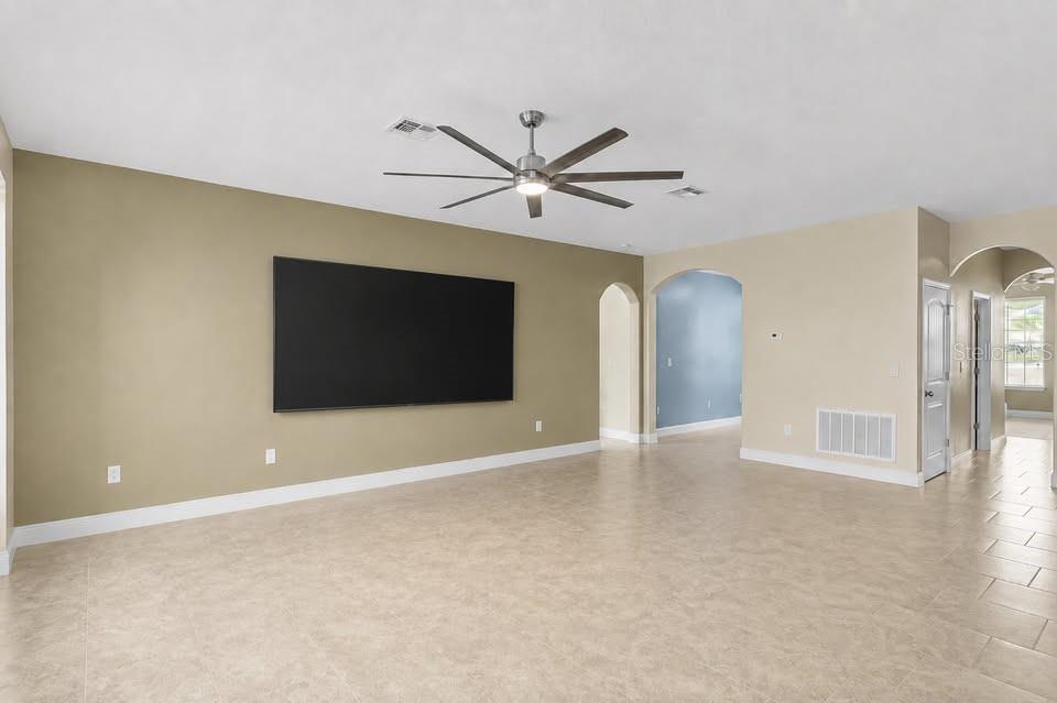 A spacious living room features beige walls, tile flooring, a ceiling fan, and a large television — 1316 LAKE BATON DRIVE, DELTONA, FL