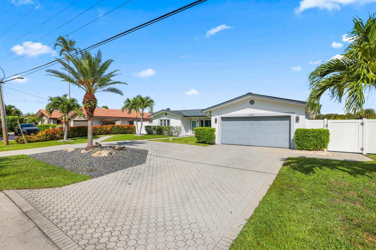 A single-story house with a gray garage, paved driveway, and palm trees in the yard — 4021 NE 27th Terrace, Lighthouse Point FL 33064, LIGHTHOUSE POINT, FL