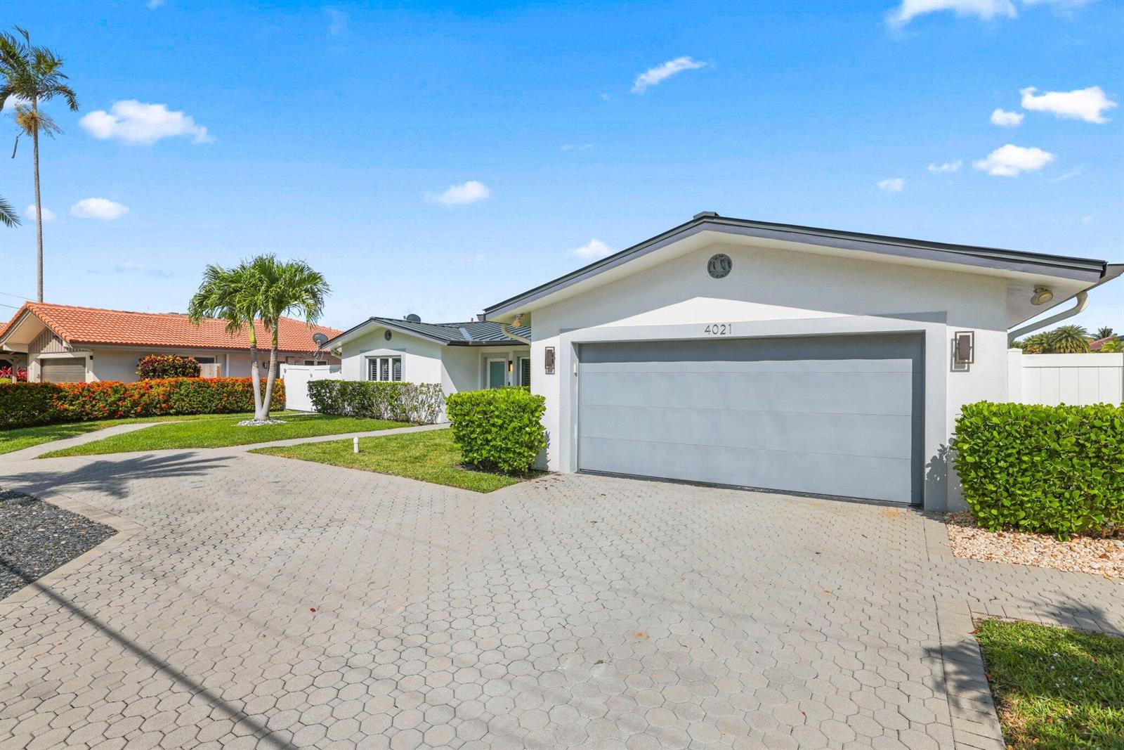 A single-story house with a gray garage door and a paved driveway under a blue sky — 4021 NE 27th Terrace, Lighthouse Point FL 33064, LIGHTHOUSE POINT, FL