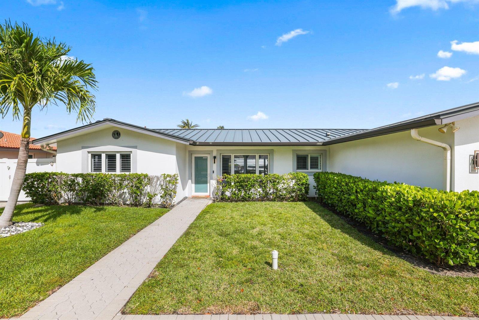 A single-story house with a metal roof, white stucco walls, and a paved walkway — 4021 NE 27th Terrace, Lighthouse Point FL 33064, LIGHTHOUSE POINT, FL
