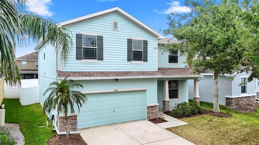 A two-story light blue house features a two-car garage, stone accents, and a front lawn — 601 19TH STREET NW, RUSKIN, FL