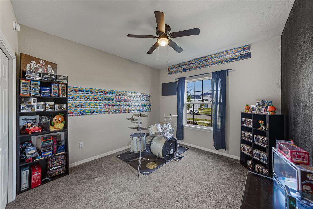 A bedroom features a drum set, two black shelving units, and walls decorated with toy cars — 929 MONTGOMERY LANE, POLK CITY, FL