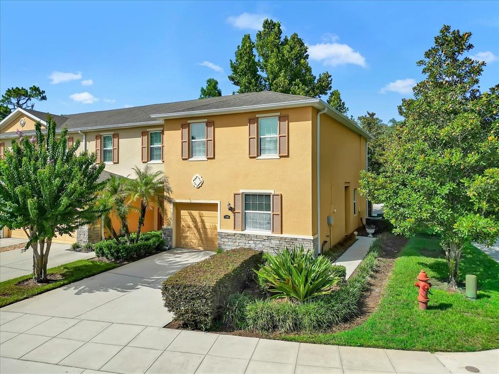 A two-story tan townhouse with a stone-accented base, a garage, and a landscaped front yard — 13901 RIVER WILLOW PLACE, TAMPA, FL