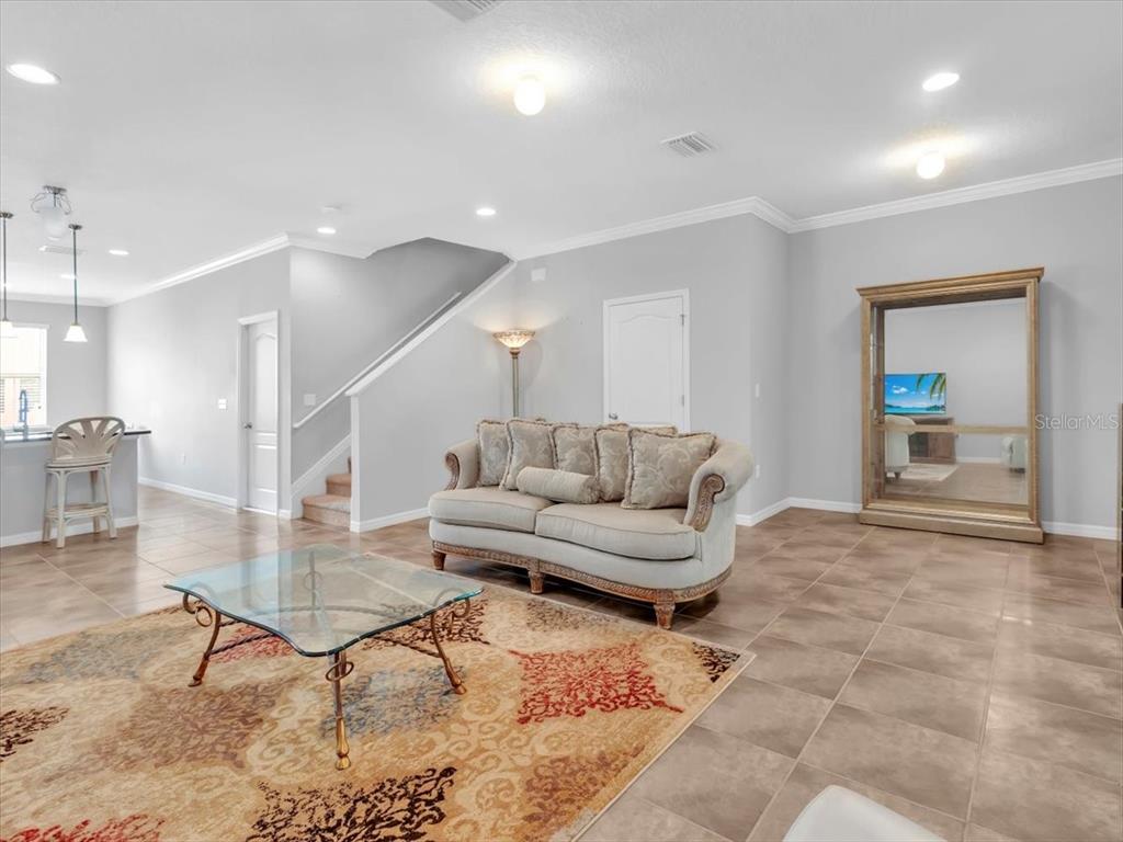 A living room with tile floors, a beige sofa, a glass coffee table, and a large mirror — 13901 RIVER WILLOW PLACE, TAMPA, FL