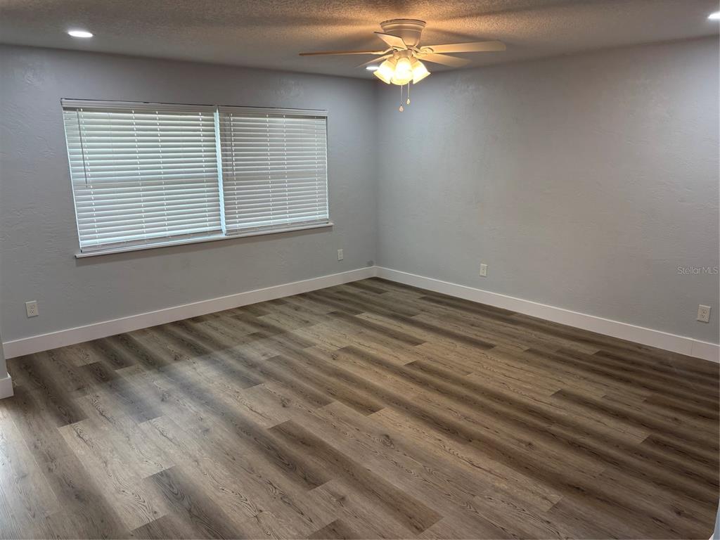 An empty room features light gray walls, wood-look flooring, a ceiling fan, and large windows — 977 E NORMANDY BOULEVARD, DELTONA, FL