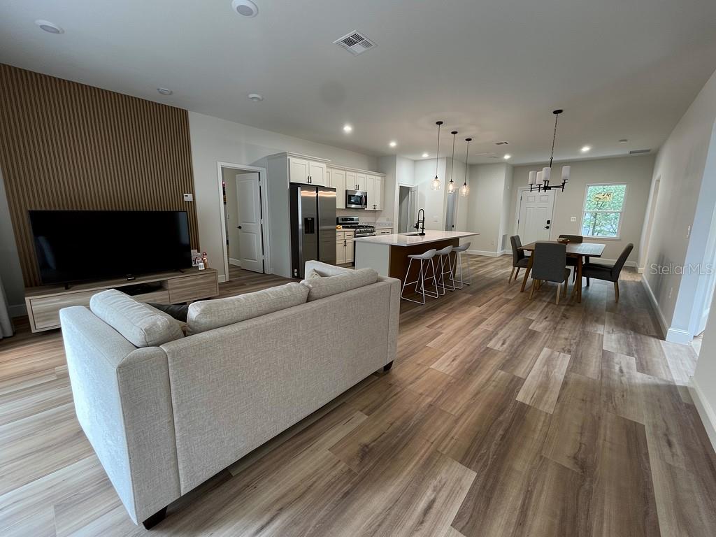 An open-concept living room and kitchen featuring wood-look flooring and a slatted wood accent wall — 3383 LOVELAND BOULEVARD, PORT CHARLOTTE, FL