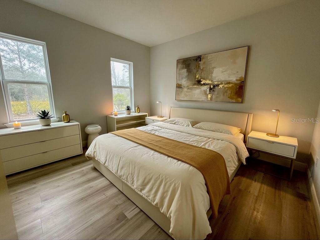 A bedroom features a platform bed, light wood flooring, two windows, and neutral wall paint — 3383 LOVELAND BOULEVARD, PORT CHARLOTTE, FL
