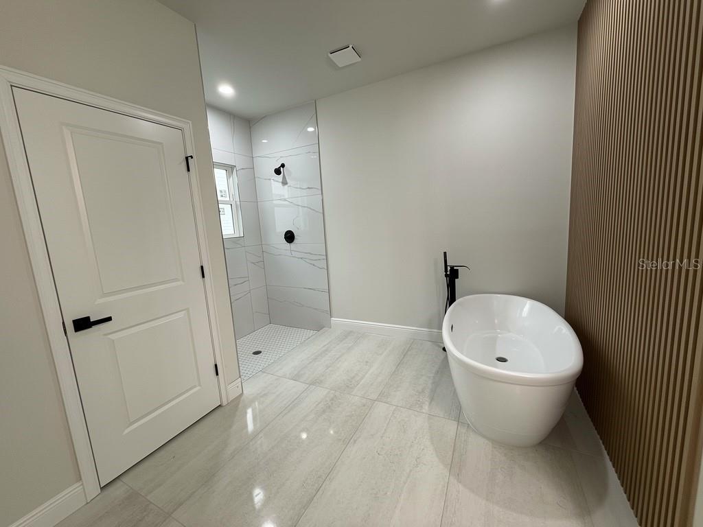 A modern bathroom features a freestanding tub, a walk-in shower, and wood-slat accent wall — 3383 LOVELAND BOULEVARD, PORT CHARLOTTE, FL