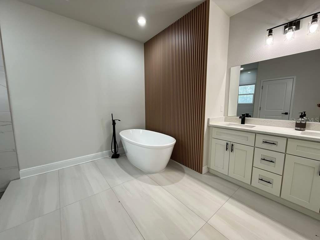 A bathroom features a freestanding tub, a wood-slat accent wall, and a double-sink vanity — 3383 LOVELAND BOULEVARD, PORT CHARLOTTE, FL