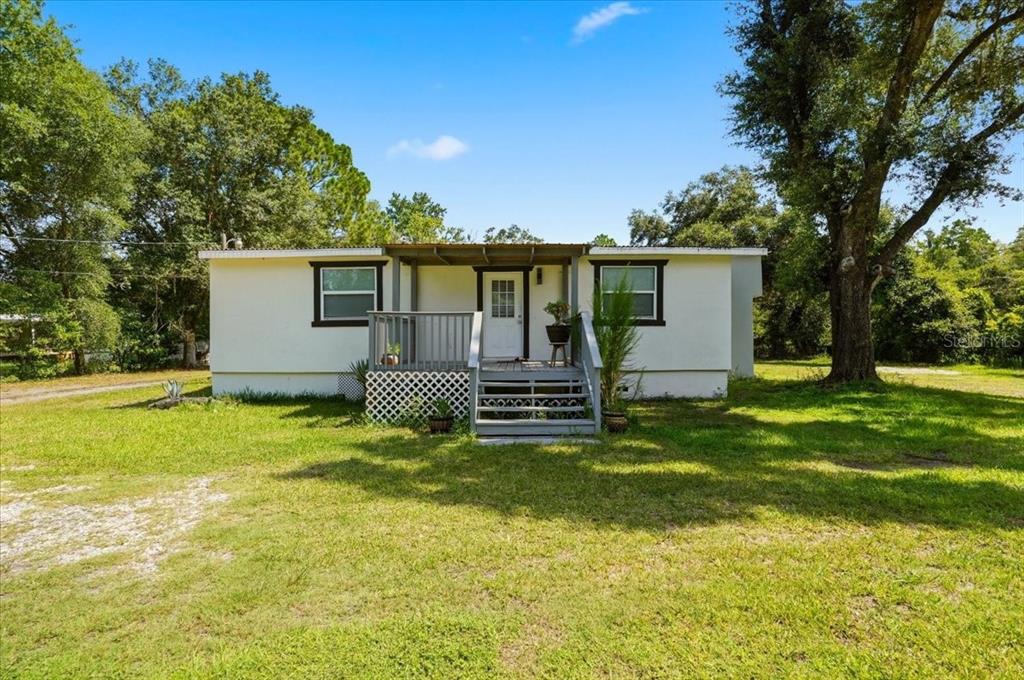 A single-story mobile home with a front porch sits on a grassy lot with trees — 303 WILDLIFE TRAIL, LAKELAND, FL