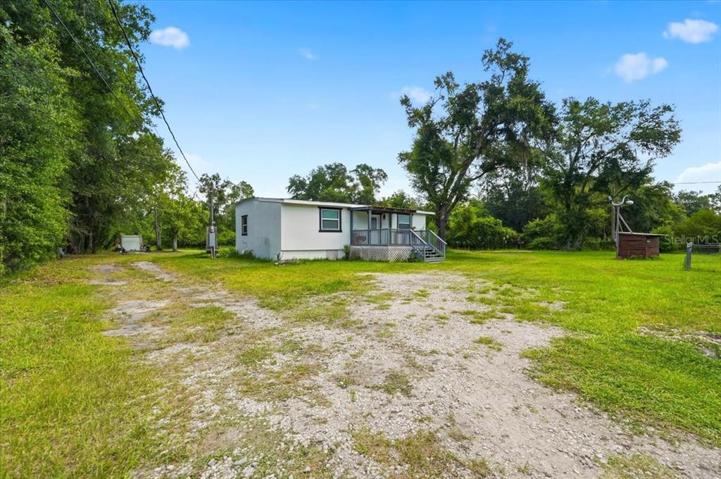 A white single-story house with a front porch sits on a large, grassy, gravel-covered lot — 303 WILDLIFE TRAIL, LAKELAND, FL