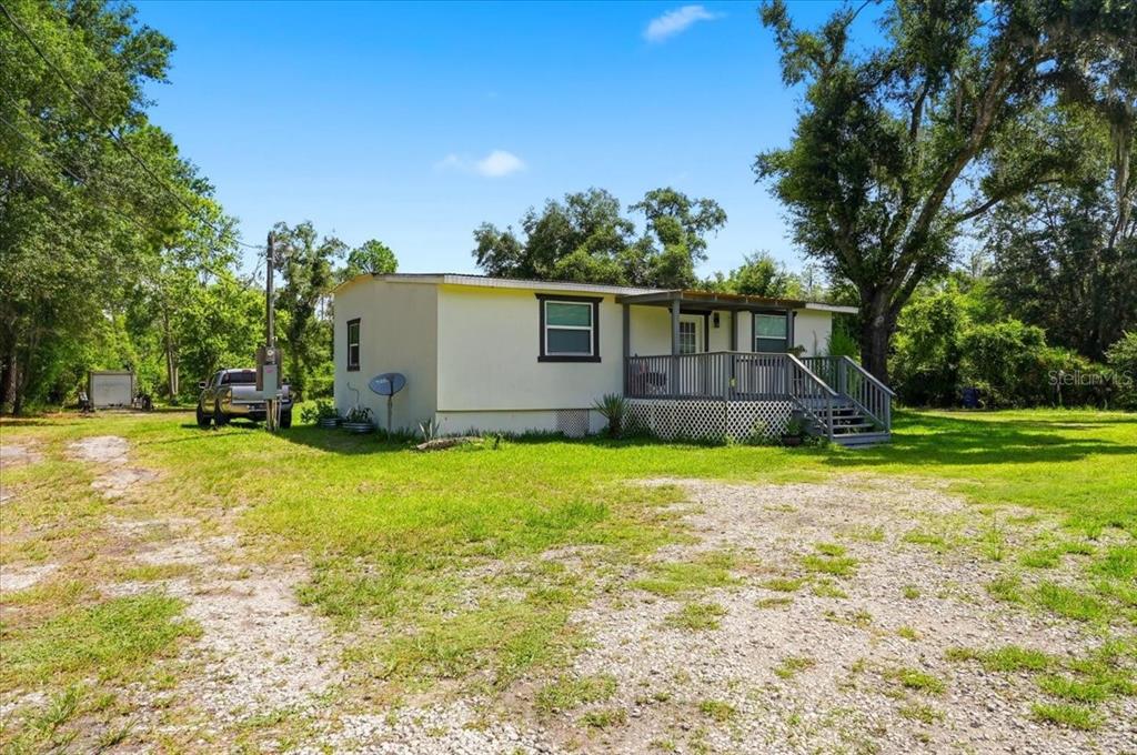 A single-story house with a front porch sits on a gravel lot surrounded by trees — 303 WILDLIFE TRAIL, LAKELAND, FL