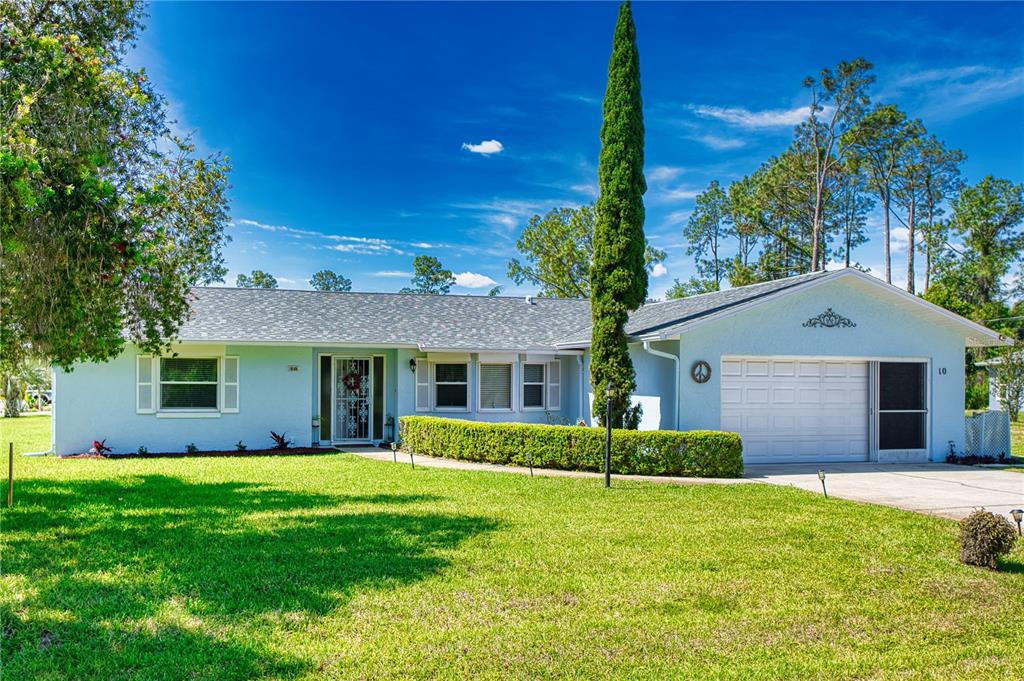 A light blue single-story house with a white garage and a tall, thin evergreen tree — 10 ROCKWELL LANE, PALM COAST, FL