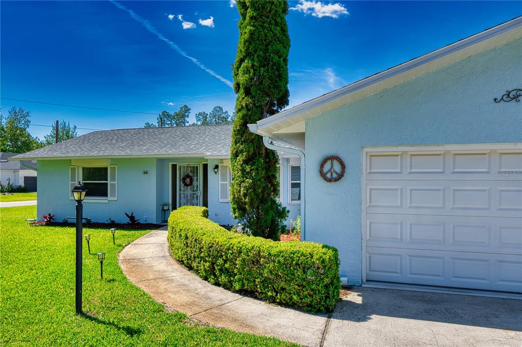 A light blue house features a curved hedge, a tall evergreen tree, and a garage — 10 ROCKWELL LANE, PALM COAST, FL