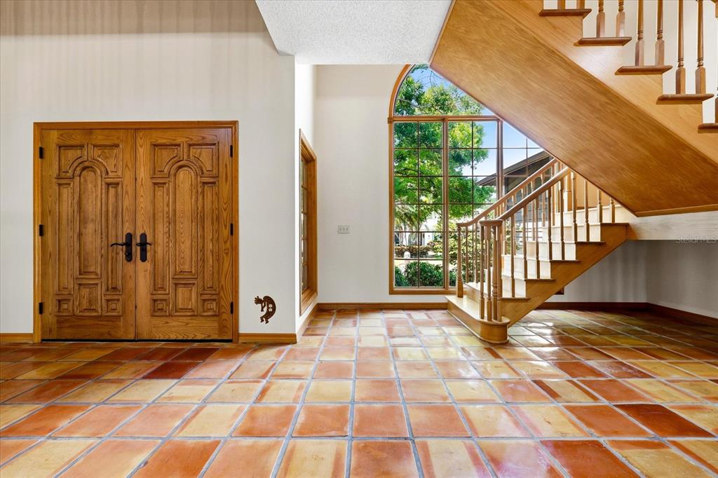 A foyer with terracotta tile flooring, a wooden double door, and a wooden staircase — 2917 SANDPIPER PLACE, CLEARWATER, FL