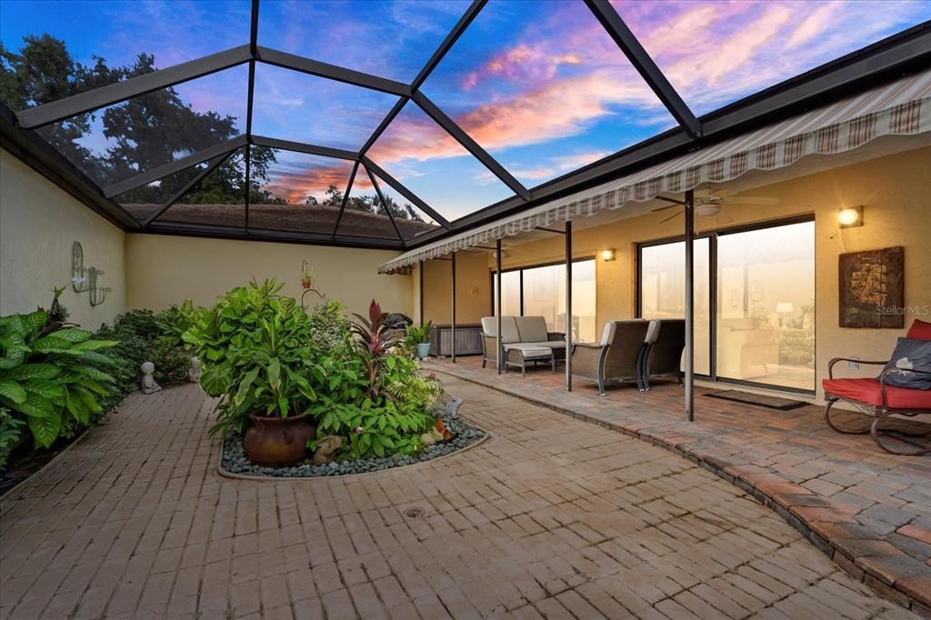 A screened-in patio features brick pavers, a central garden bed, and outdoor seating — 3953 GLEN OAKS MANOR DRIVE, SARASOTA, FL