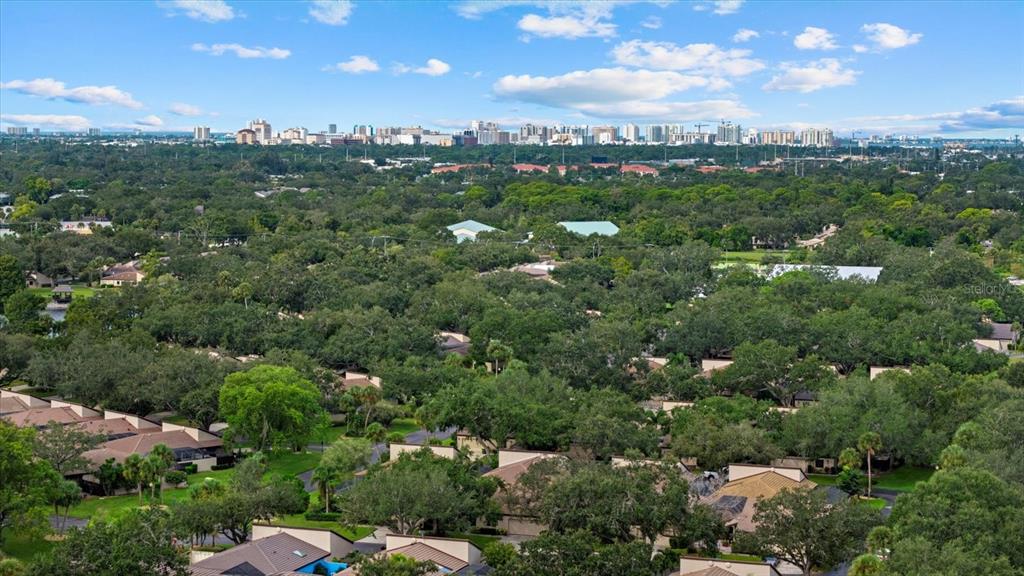 An aerial view shows a residential neighborhood with many trees and a distant city skyline — 3953 GLEN OAKS MANOR DRIVE, SARASOTA, FL