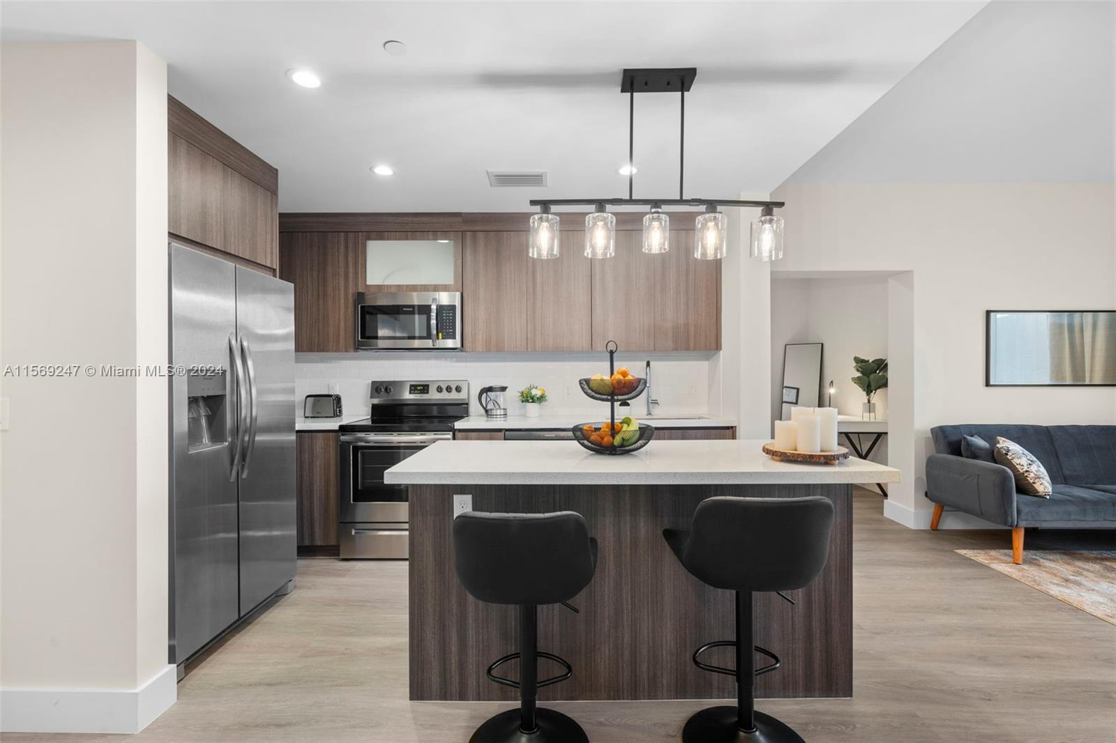 A modern kitchen features wood-toned cabinetry, stainless steel appliances, a central island, and bar seating — 1938 Jackson St # 306, Hollywood FL 33020, HOLLYWOOD, FL