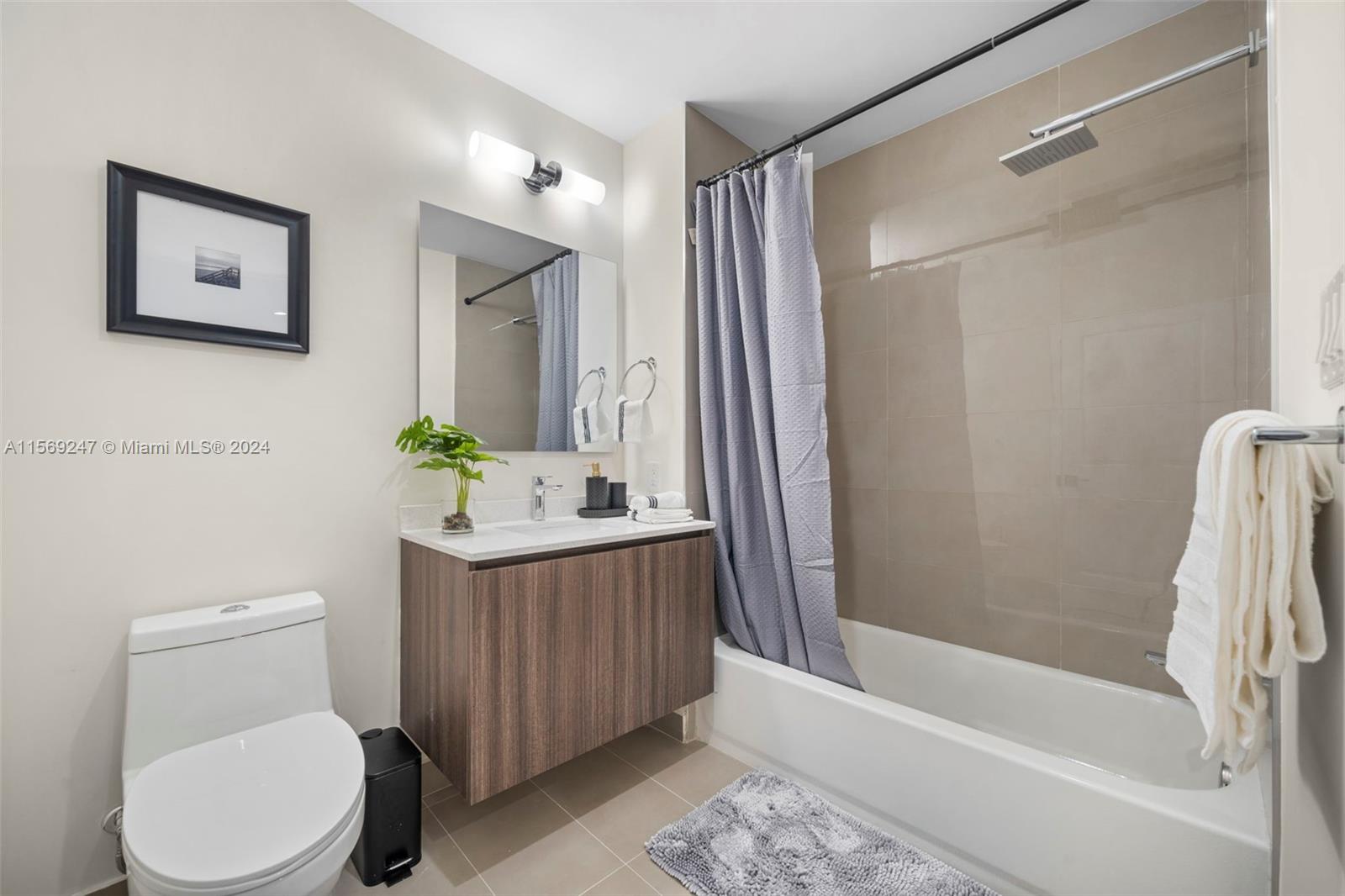 A bathroom features a wood-toned vanity, a toilet, and a shower-tub combination with beige tiles — 1938 Jackson St # 306, Hollywood FL 33020, HOLLYWOOD, FL
