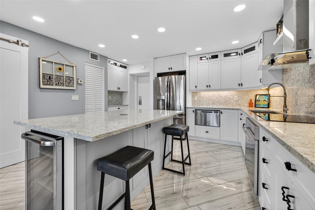 A modern kitchen features white cabinetry, granite countertops, a central island, and light-colored tile flooring — 4900 BRITTANY DRIVE S UNIT 409, ST PETERSBURG, FL