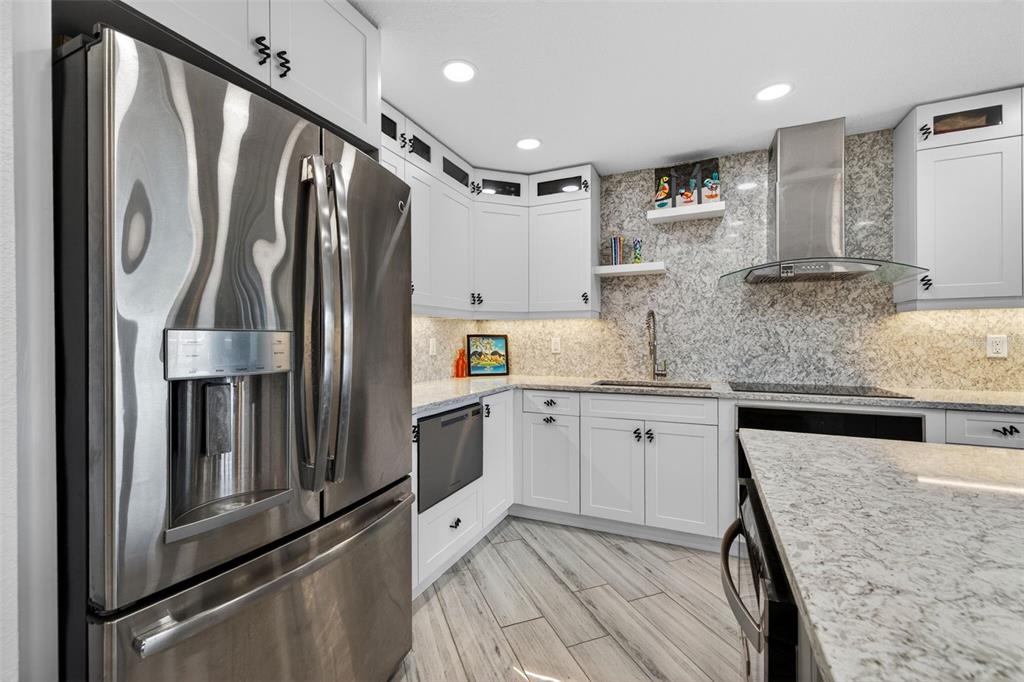 A modern kitchen features white cabinets, granite countertops, stainless steel appliances, and wood-look tile flooring — 4900 BRITTANY DRIVE S UNIT 409, ST PETERSBURG, FL