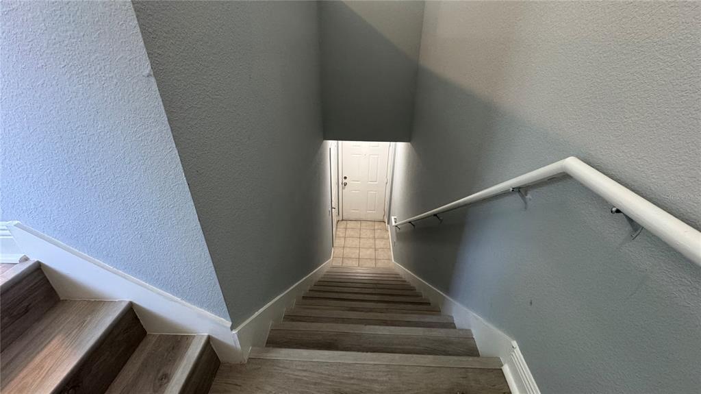 A staircase with wood-look steps and a white handrail leads down to a tiled landing — 234 SOUTHERN PECAN CIRCLE UNIT 202, WINTER GARDEN, FL