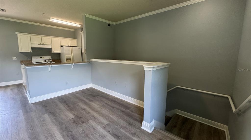A kitchen with white cabinets and a breakfast bar overlooks a staircase with railings — 234 SOUTHERN PECAN CIRCLE UNIT 202, WINTER GARDEN, FL