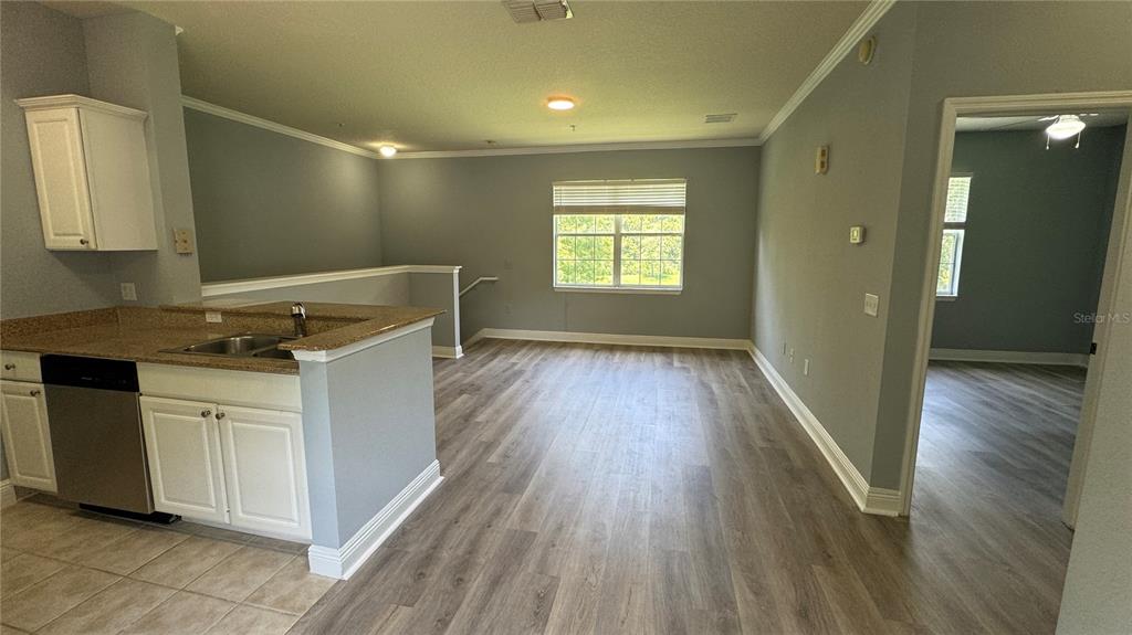 A kitchen with granite countertops overlooks an open living area with light wood flooring — 234 SOUTHERN PECAN CIRCLE UNIT 202, WINTER GARDEN, FL