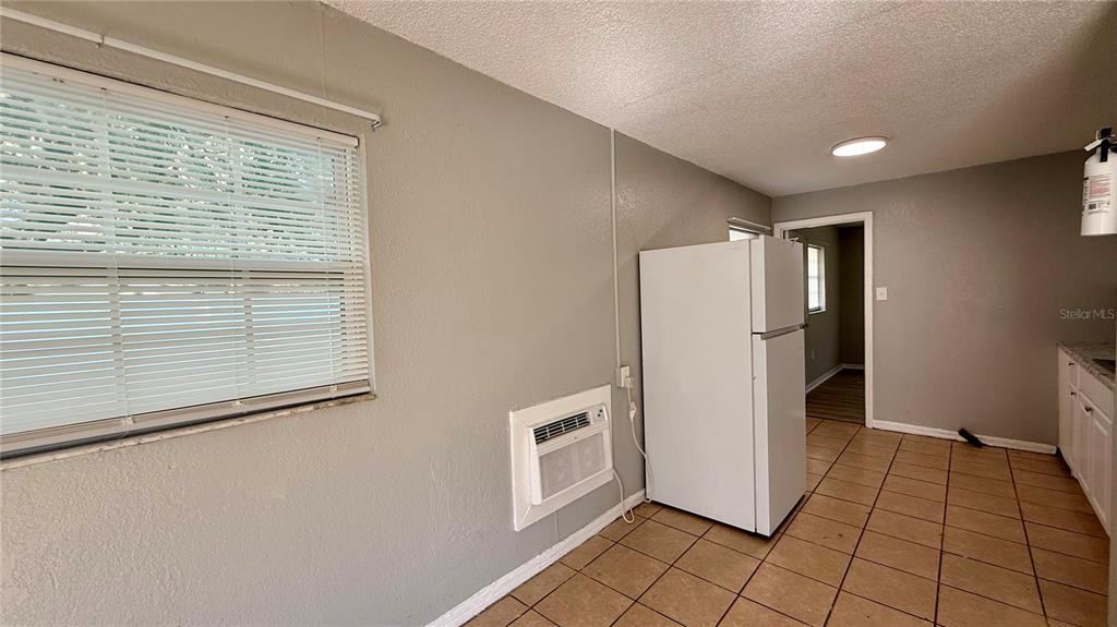 A kitchen features a white refrigerator, a wall-mounted air conditioner, and tiled flooring — 205 MILL STREET, WILDWOOD, FL