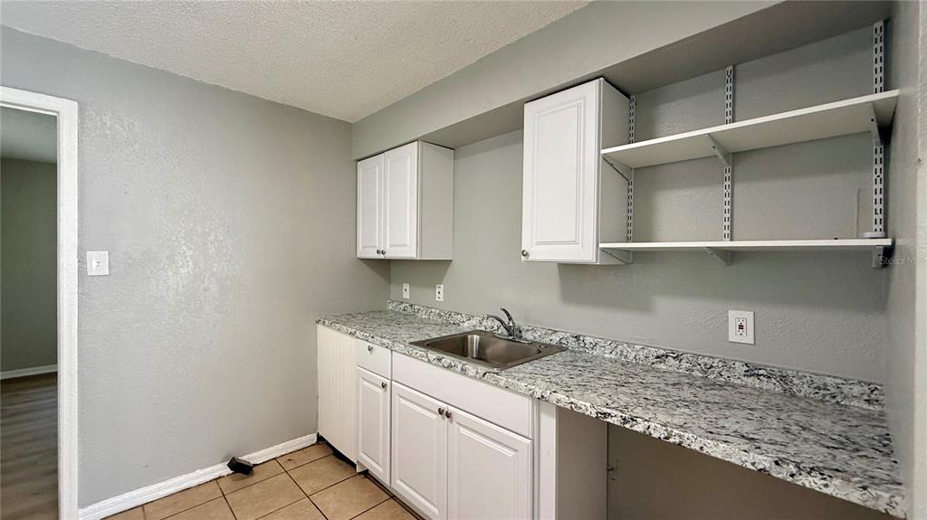 A kitchen features white cabinets, granite countertops, an undermount sink, and open wall shelving — 205 MILL STREET, WILDWOOD, FL