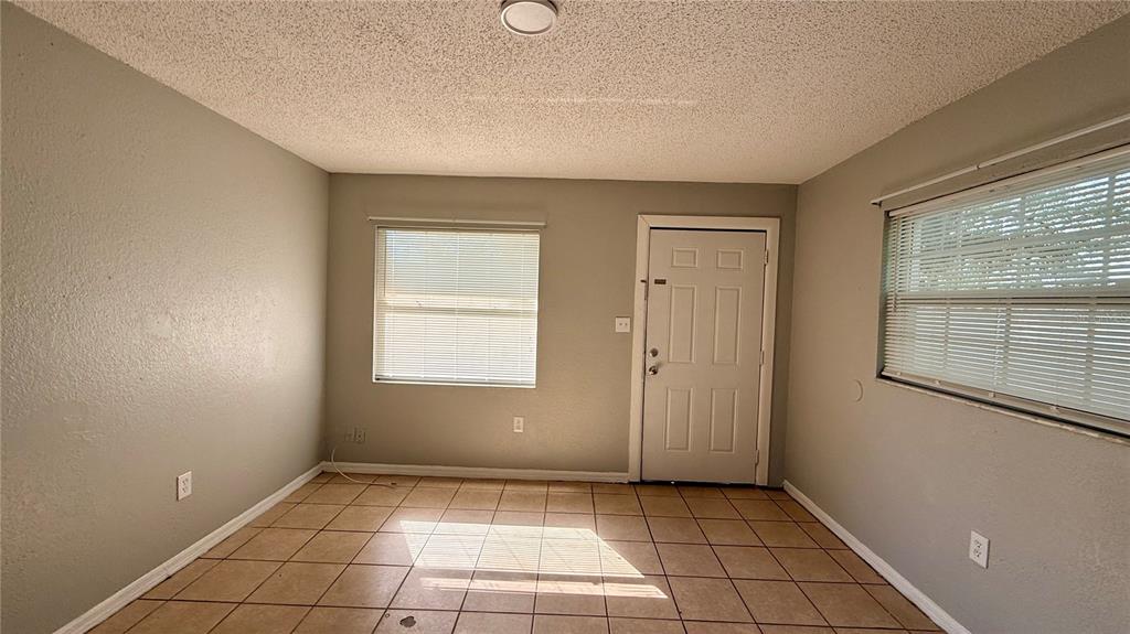 An empty room with beige walls, tile flooring, two windows with blinds, and a door — 205 MILL STREET, WILDWOOD, FL