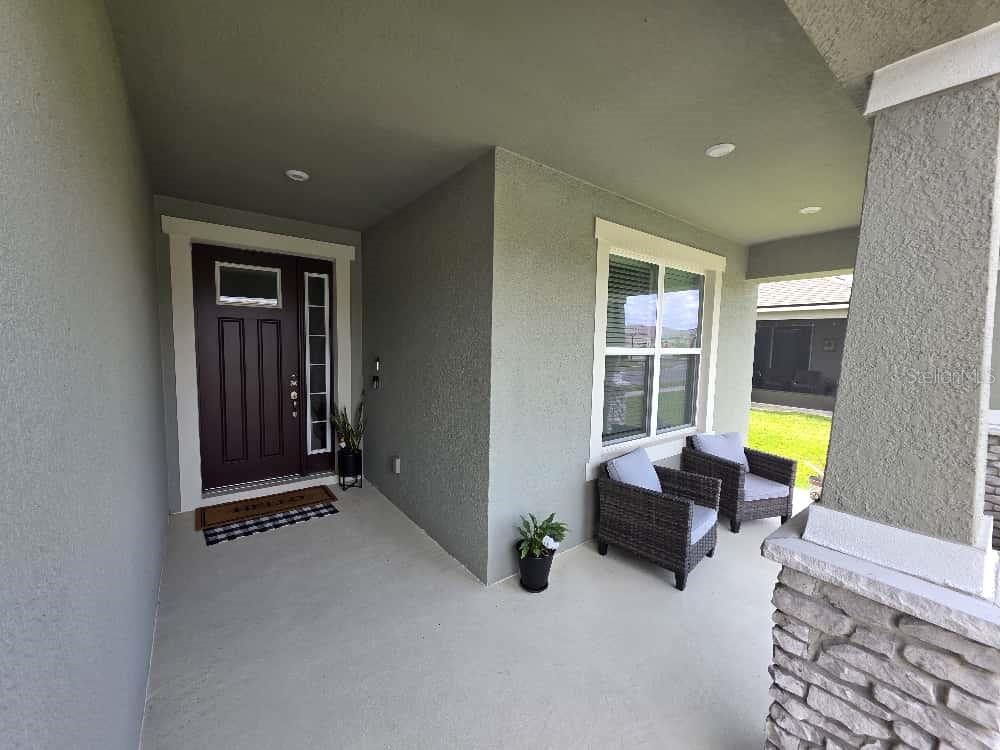 A covered front porch features a dark door, two wicker chairs, and stone column accents — 1791 SMARTS RULE STREET, KISSIMMEE, FL