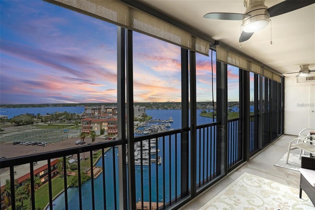 A balcony with a ceiling fan overlooks a marina and water at sunset — 10355 PARADISE BOULEVARD UNIT 1010-1011, ST PETERSBURG, FL