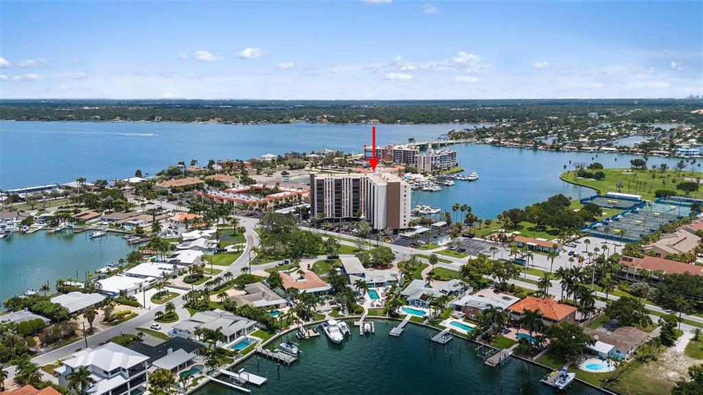 An aerial view shows a tall apartment building surrounded by water, docks, and residential homes — 10355 PARADISE BOULEVARD UNIT 1010-1011, ST PETERSBURG, FL