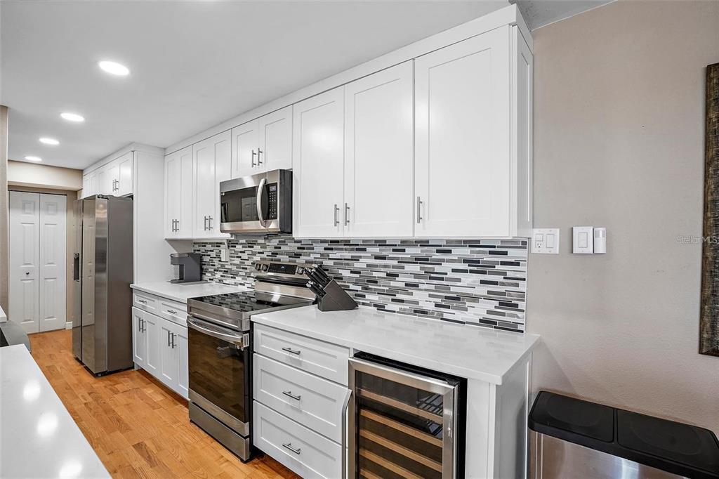 A kitchen features white cabinets, stainless steel appliances, a tiled backsplash, and wood flooring — 10355 PARADISE BOULEVARD UNIT 1010-1011, ST PETERSBURG, FL