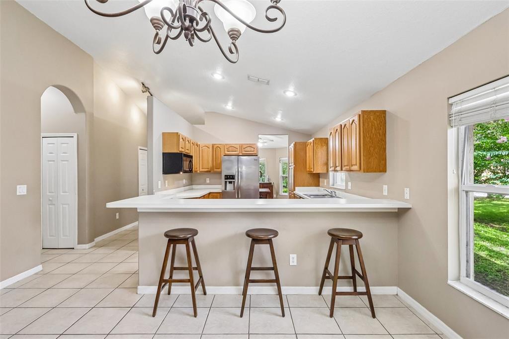 A kitchen features wooden cabinets, a white breakfast bar with three stools, and tile flooring — 619 CORAL WAY, WINTER SPRINGS, FL