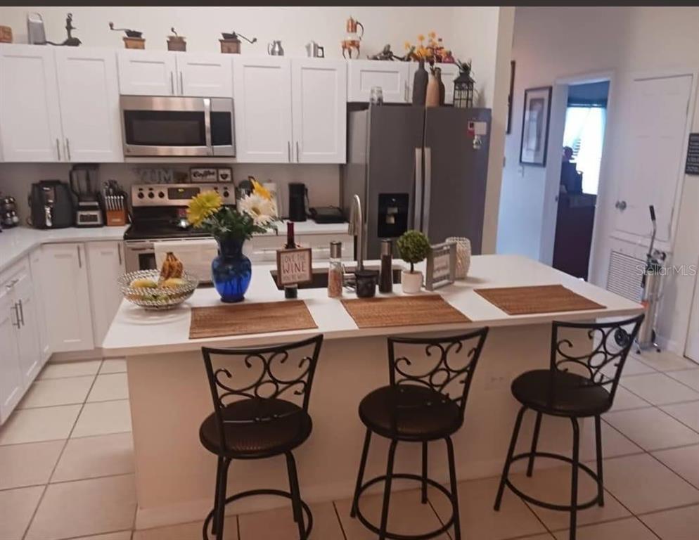 A kitchen with white cabinets, stainless steel appliances, a center island, and three bar stools — 2409 MING COURT, KISSIMMEE, FL