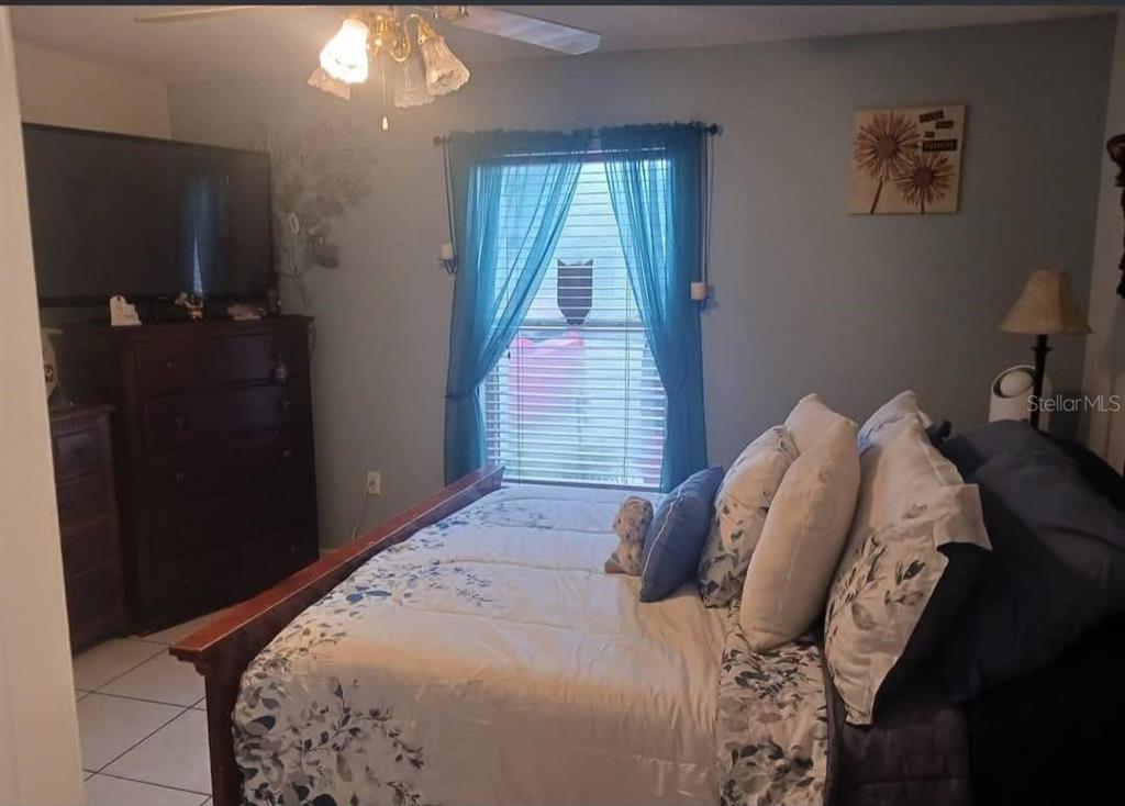 A bedroom features a bed with floral bedding, a dark wood dresser, and blue curtains — 2409 MING COURT, KISSIMMEE, FL