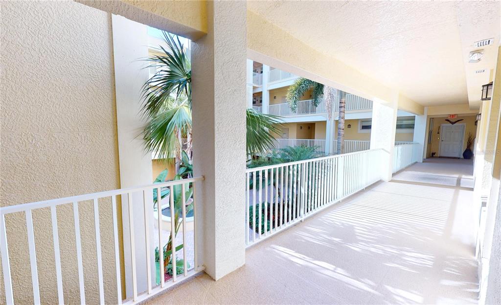 An outdoor covered walkway features white railings and views of a landscaped courtyard with palms — 255 W END DRIVE UNIT 3206, PUNTA GORDA, FL