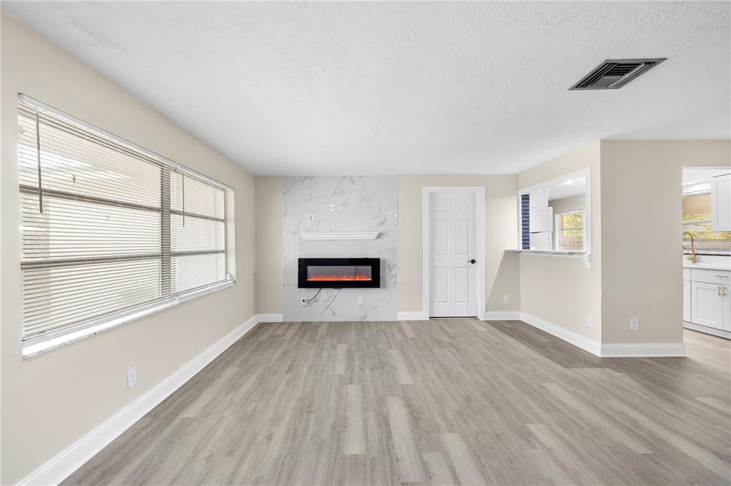 A living room with light wood-look flooring, a marble-tiled fireplace, and a kitchen pass-through window — 1820 PATLIN CIRCLE N, LARGO, FL
