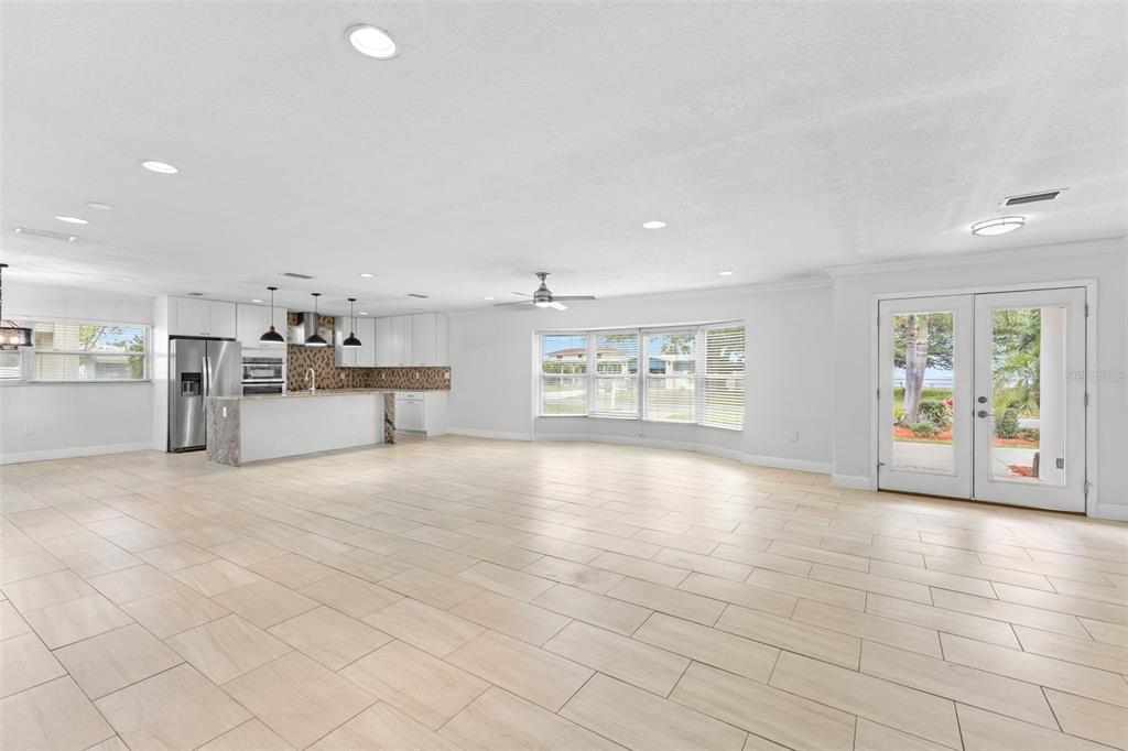 A bright, open-concept kitchen and living area featuring white cabinetry, tile flooring, and French doors — 125 CARLYLE DRIVE, PALM HARBOR, FL