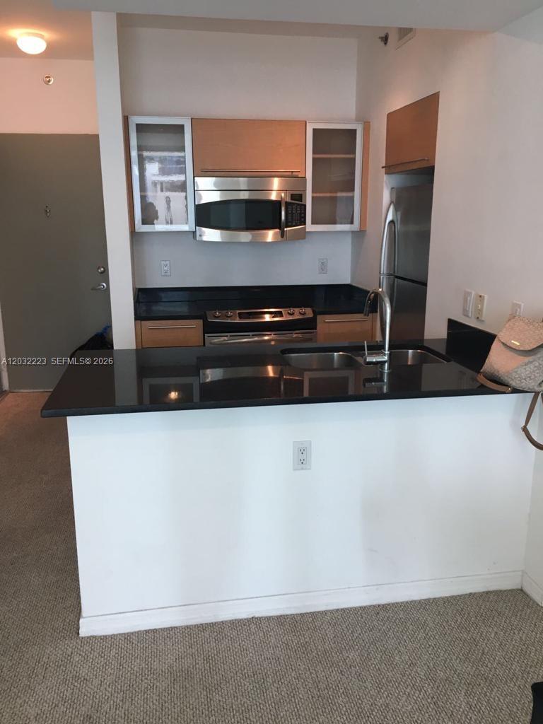 A kitchen features stainless steel appliances, light wood cabinets, and a black countertop breakfast bar — 950 Brickell Bay Dr # 701, Miami FL 33131, MIAMI, FL