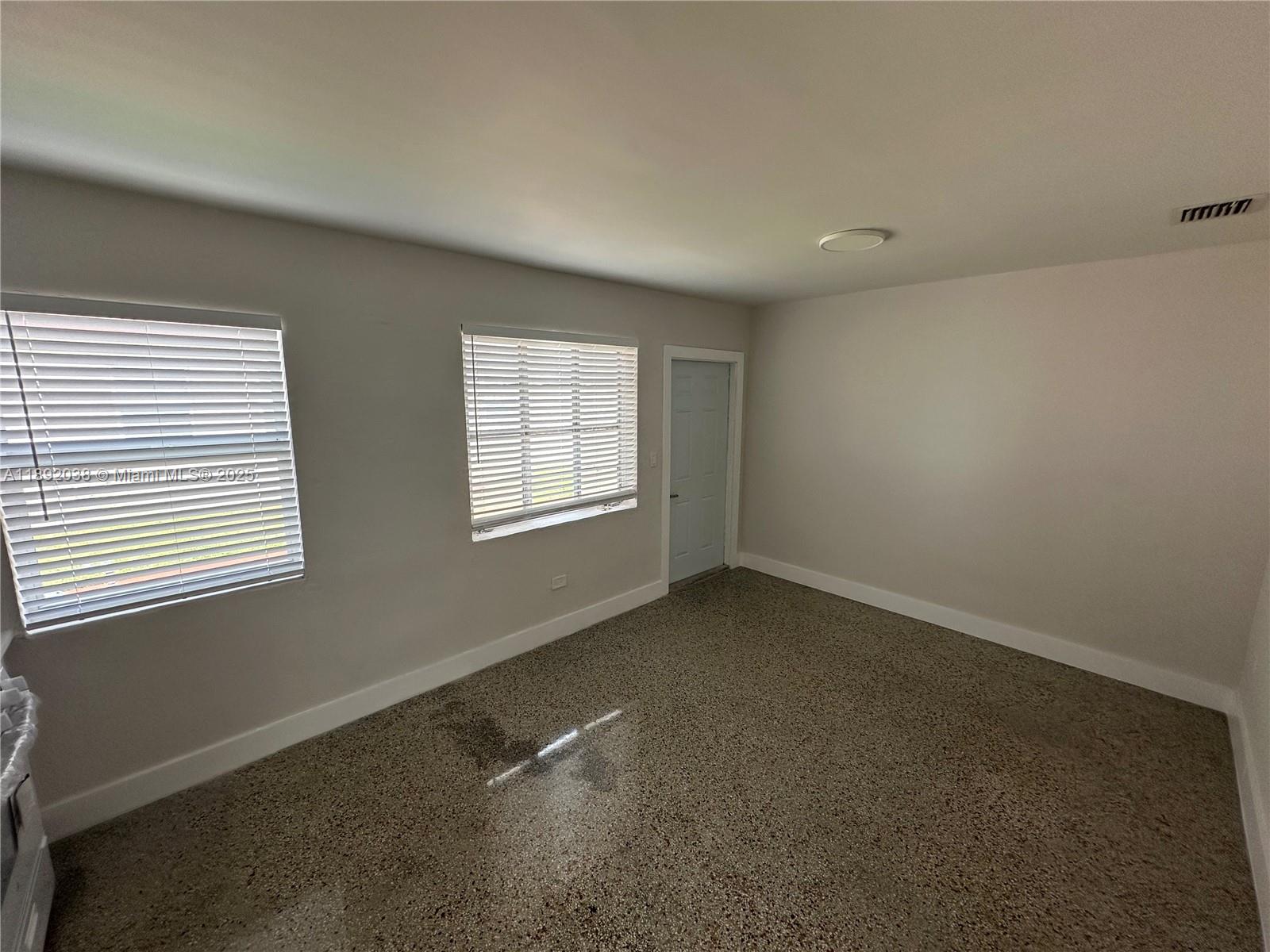 An empty room features light-colored walls, two windows with blinds, a door, and speckled flooring — 211 SW 18th Ave # 2, Miami FL 33135, MIAMI, FL