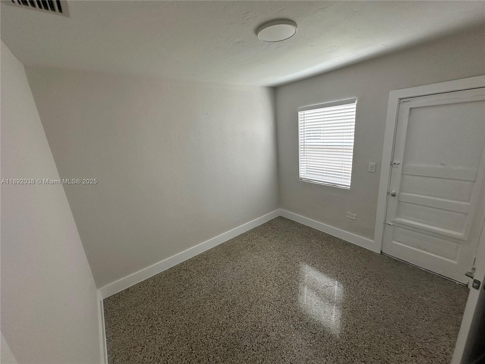 An empty room features light gray walls, a window with blinds, and speckled flooring — 211 SW 18th Ave # 2, Miami FL 33135, MIAMI, FL