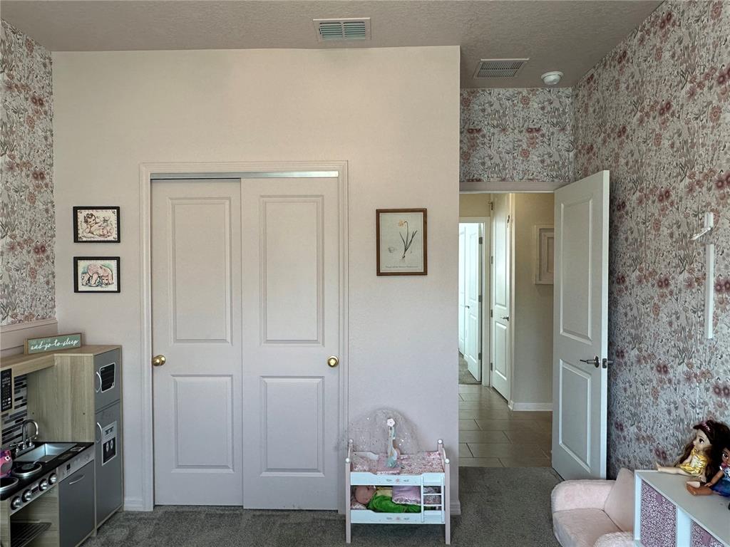 A bedroom features floral wallpaper, a white closet, and a doorway leading to a hallway — 751 STAFFORA STREET, HAINES CITY, FL