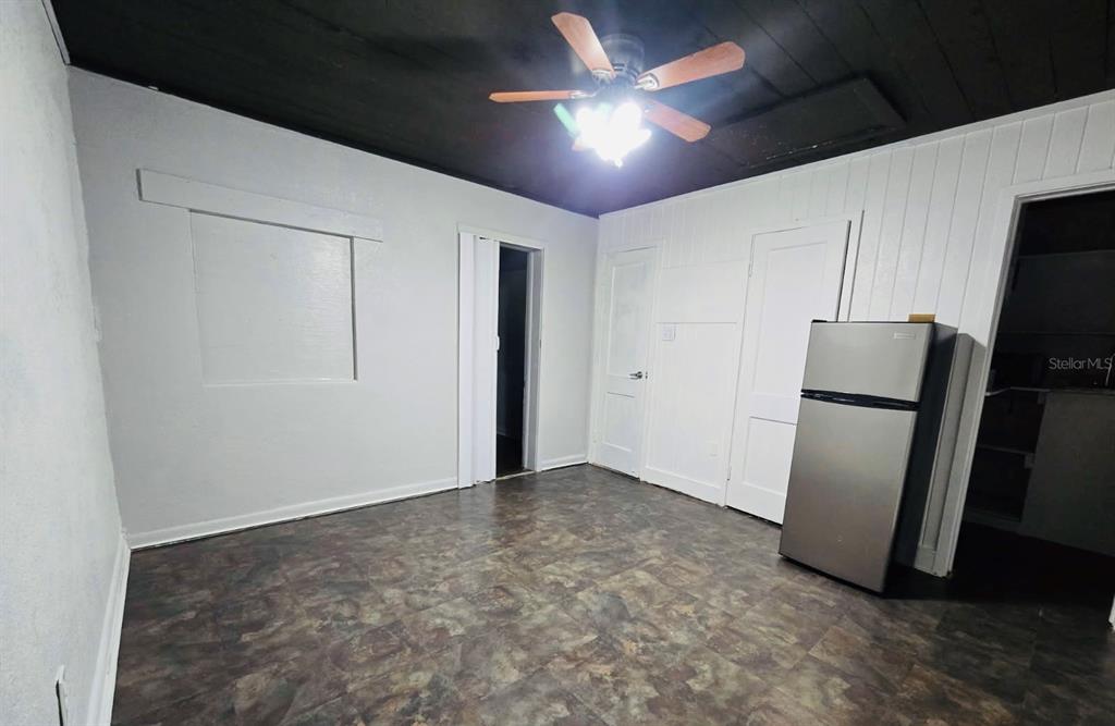 A room with a dark ceiling, white walls, vinyl flooring, and a stainless steel refrigerator — 8010 SE US HIGHWAY 301 UNIT 2A, HAWTHORNE, FL